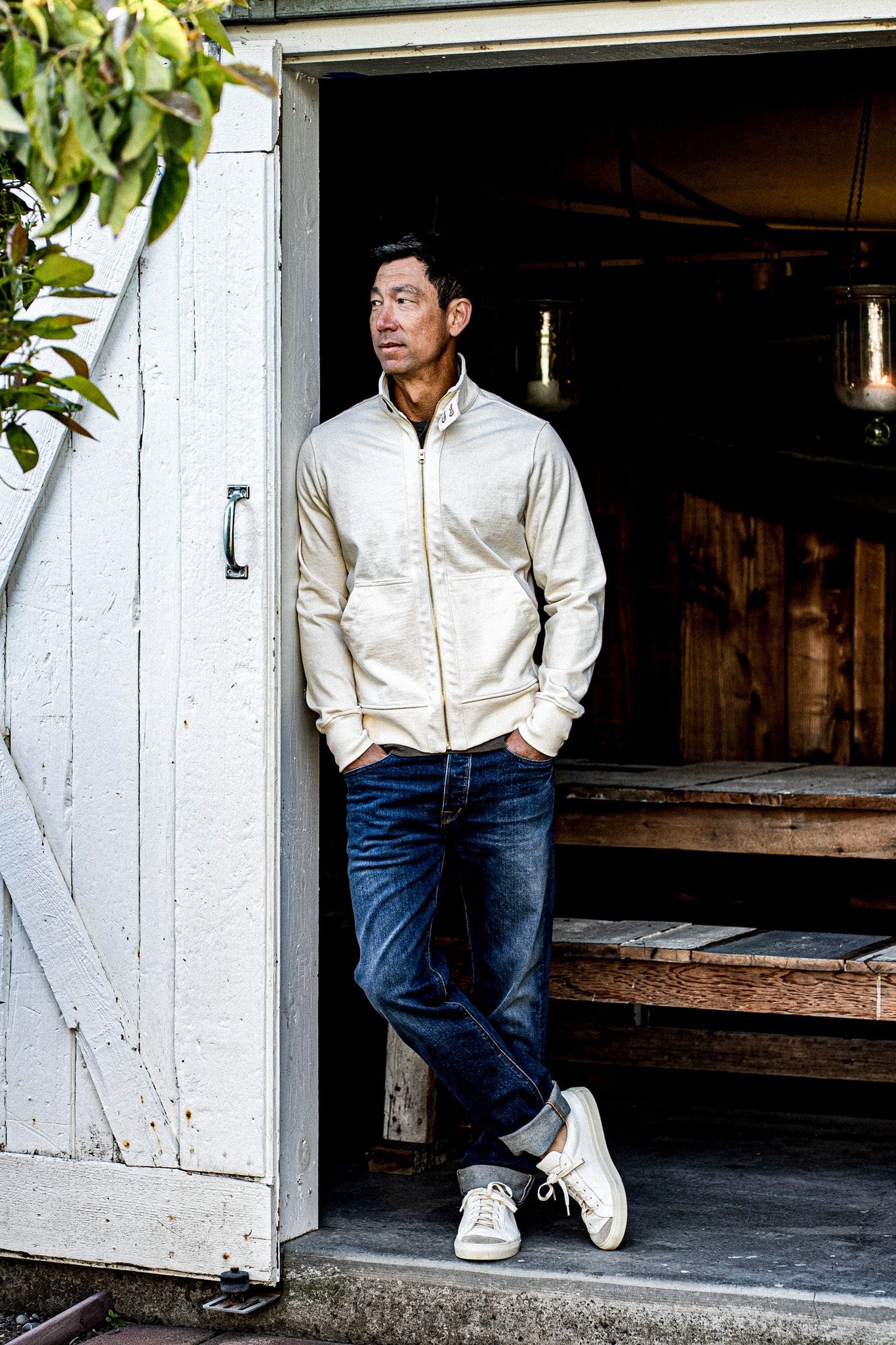 Man in a natural cotton moto zip jacket leaning in a rustic barn doorway.