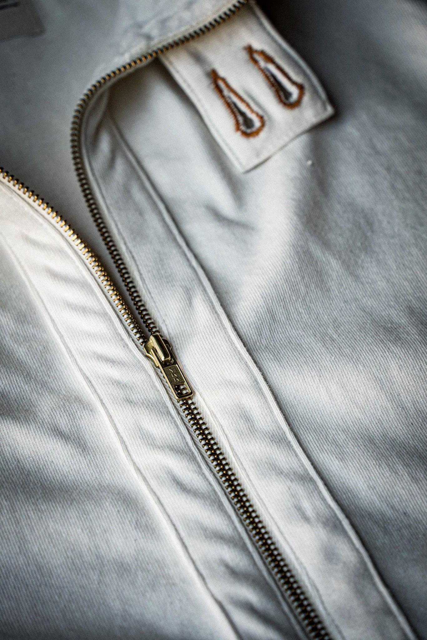 Solid brass zipper and double-stitched placket detail on a natural cotton moto jacket.