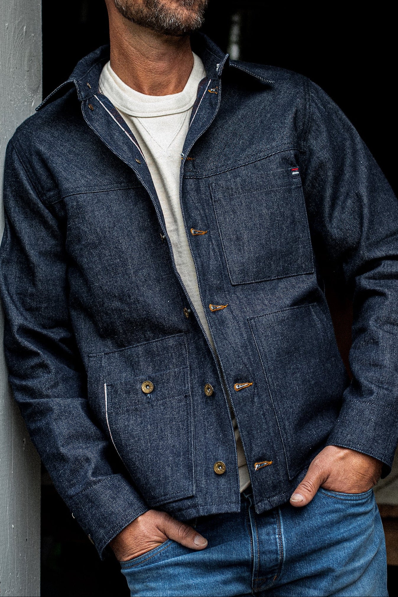 Man wearing the WiesMade Nico indigo denim jacket open over a cream sweatshirt, front torso view.