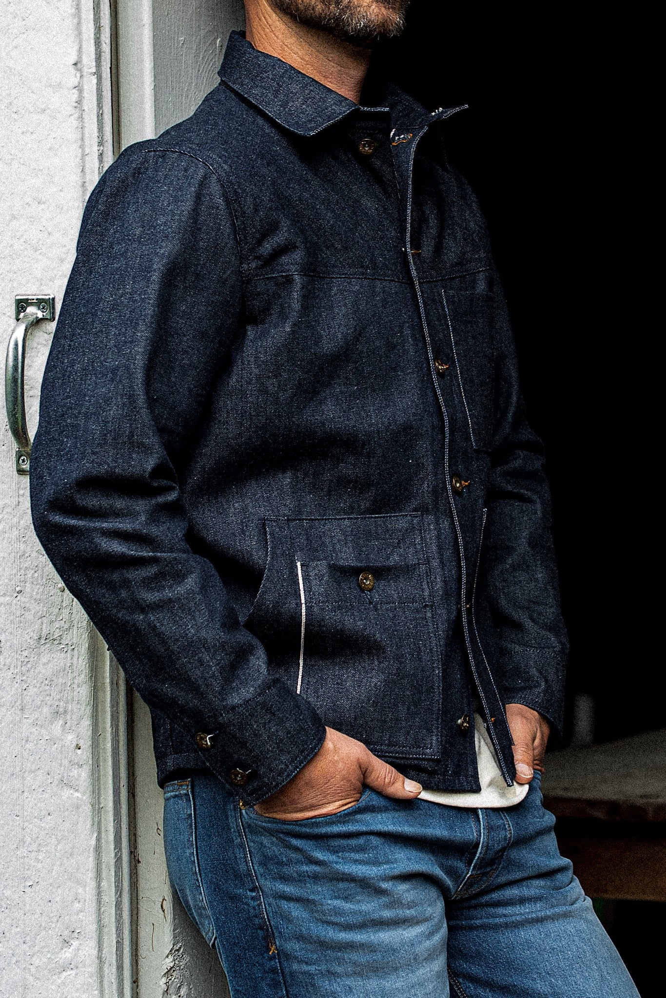 Man leaning against a wall wearing the WiesMade Nico indigo denim jacket, three-quarter view.