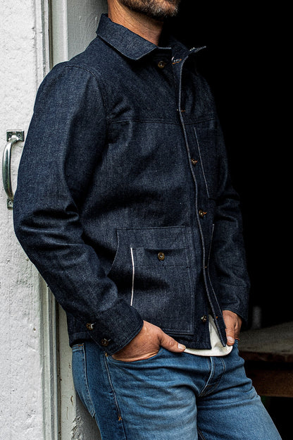 Man leaning against a wall wearing the WiesMade Nico indigo denim jacket, three-quarter view.