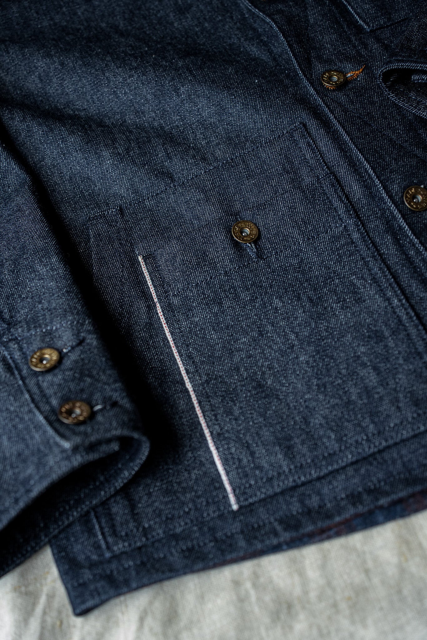 WiesMade Nico indigo denim jacket flat lay detail showing brass buttons and selvedge seam construction.
