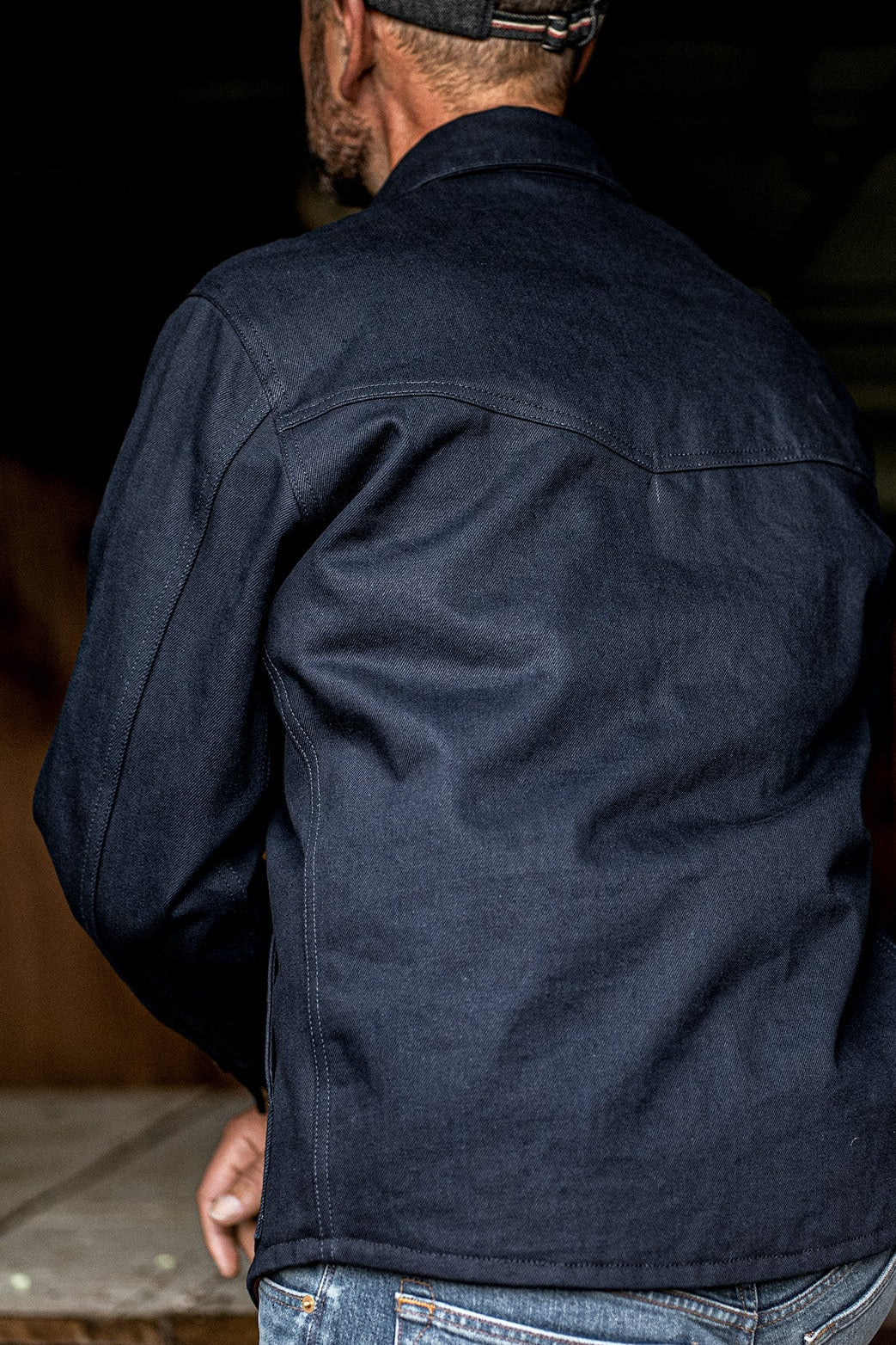 Back view of a man wearing the WiesMade Nico navy denim jacket with a ball cap.