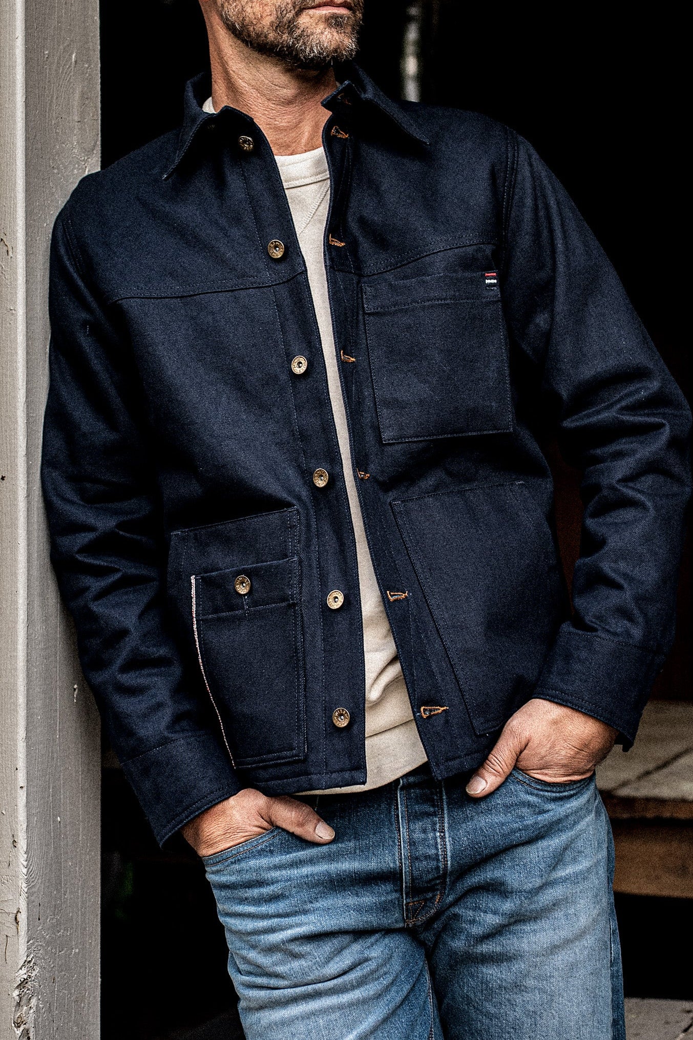 Front torso view of man wearing the WiesMade Nico navy denim jacket with brass buttons and four pockets.