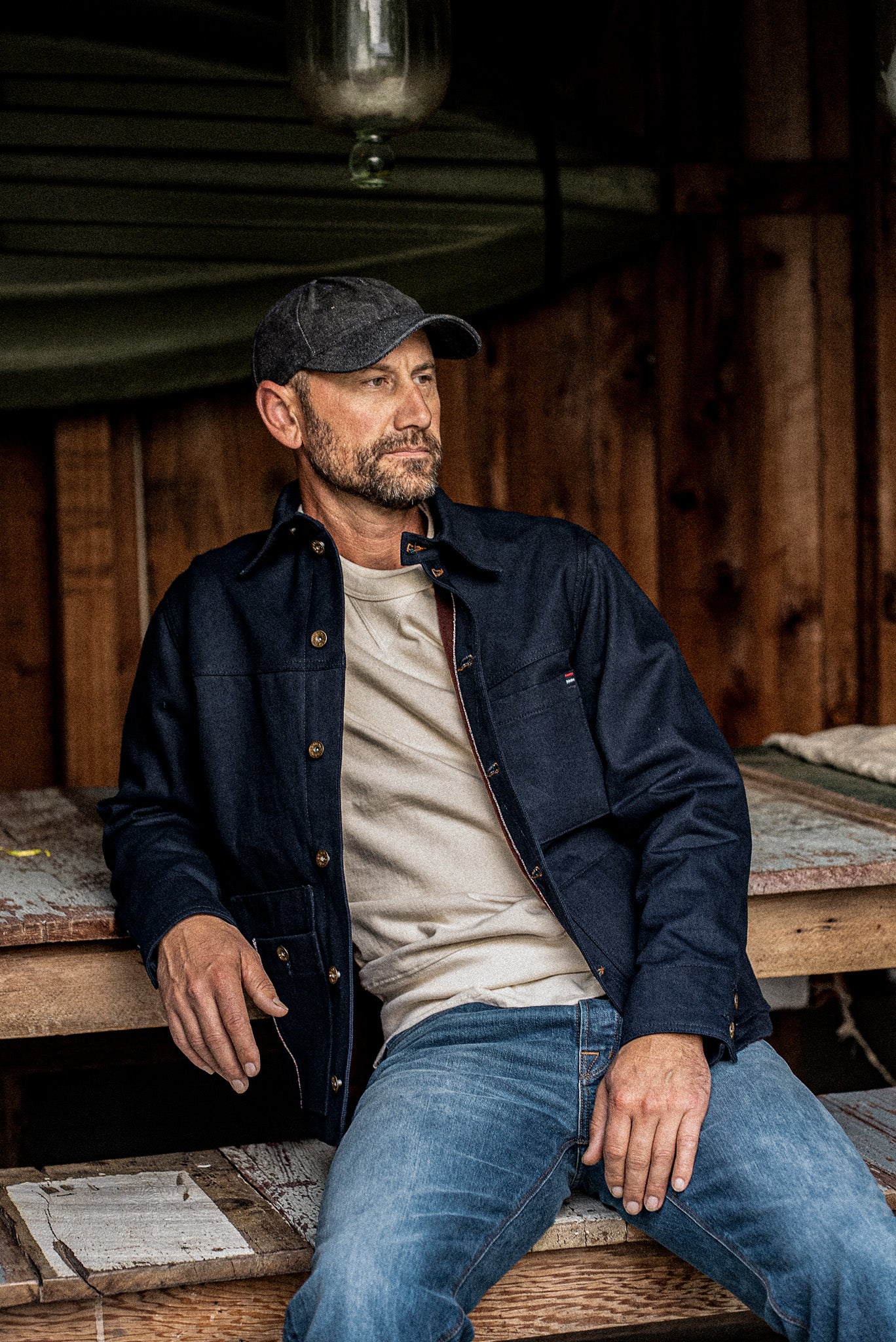 Man seated at a wooden table wearing the WiesMade Nico navy denim jacket over a cream sweatshirt.