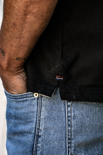 Close-up of the black Stinson rugby jersey hem with red, white, and blue side tag, worn over light-wash denim jeans.