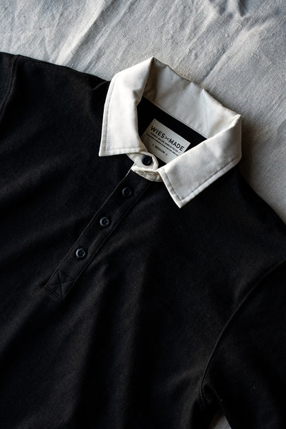 Close-up of black cotton rugby jersey with white twill collar, button placket, and WiesMade label.