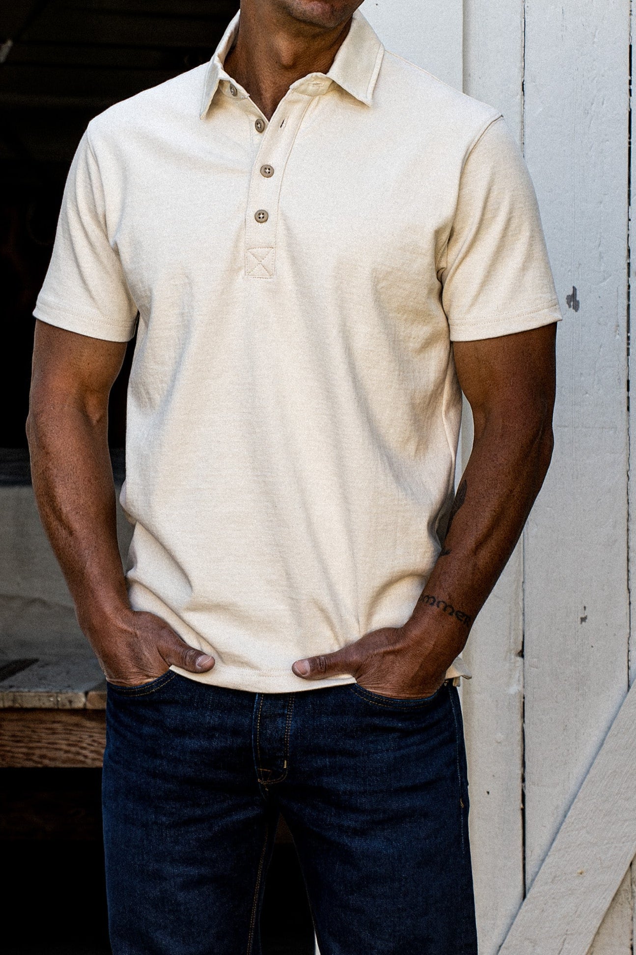 Model in a natural rugby jersey, short sleeves and buttoned placket, paired with dark jeans.