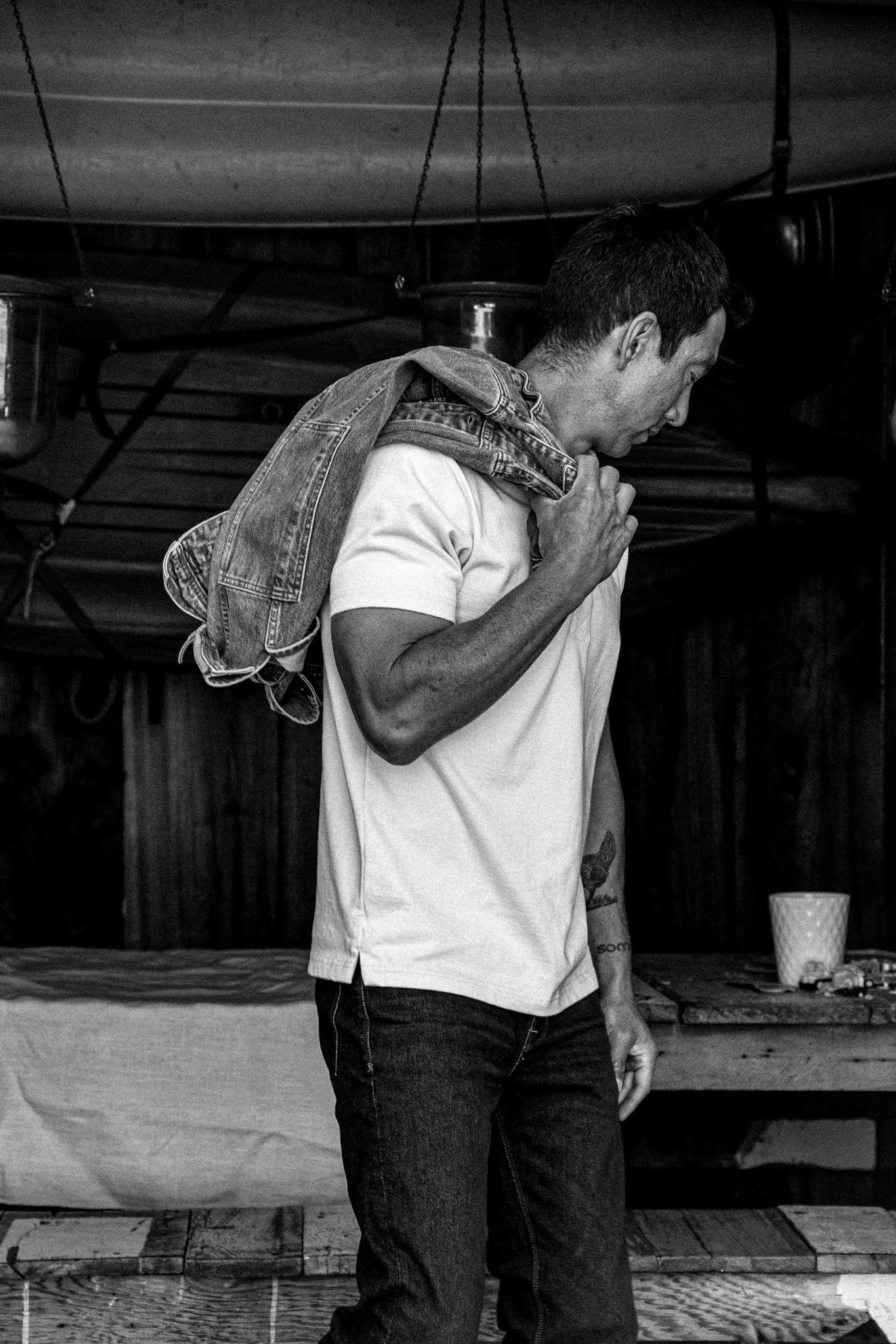 Man in profile wearing a natural cotton rugby tee, denim jacket slung over one shoulder.