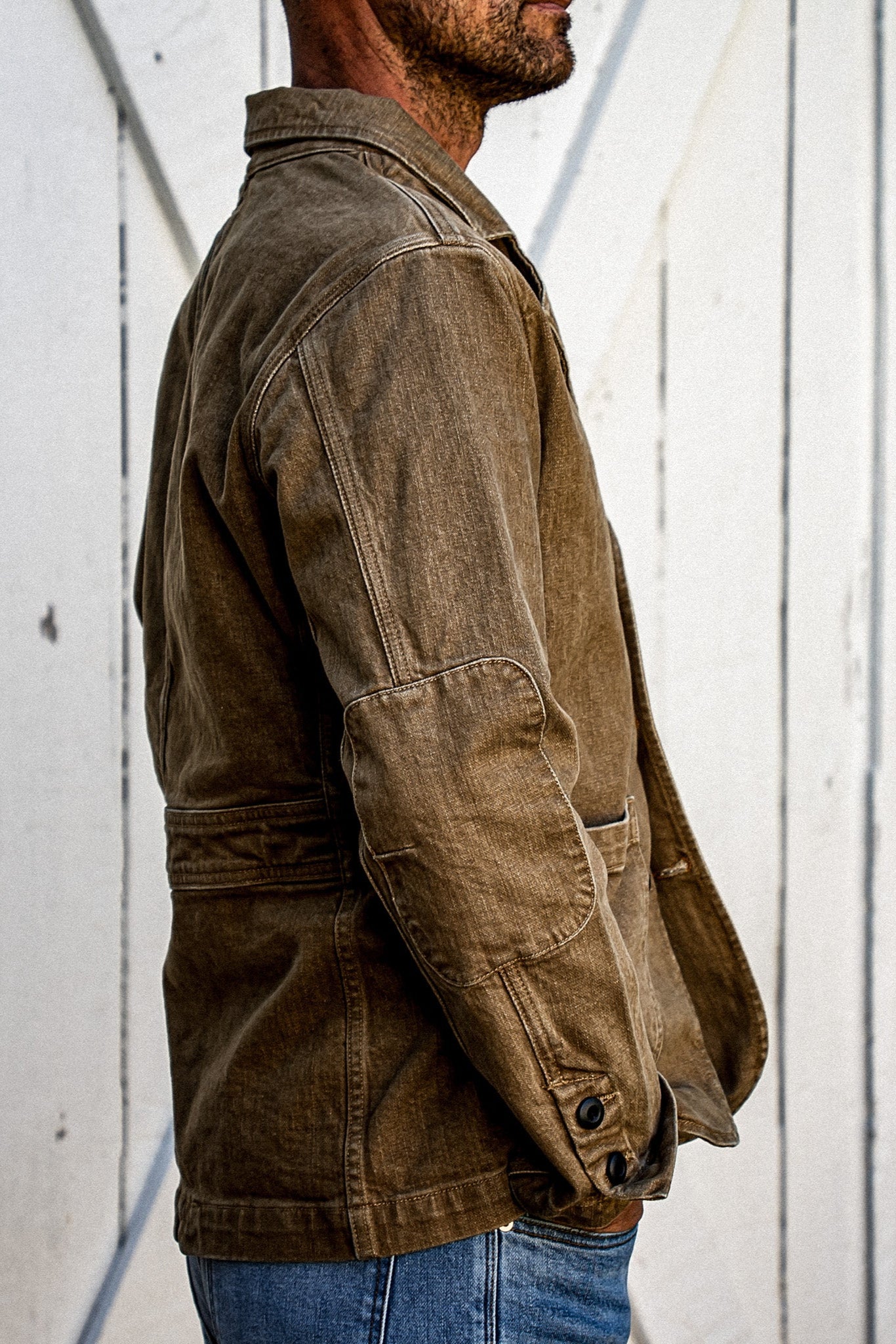 Side view of wheat denim chore blazer showing elbow patch and buttoned cuff detail.