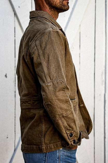 Side view of wheat denim chore blazer showing elbow patch and buttoned cuff detail.