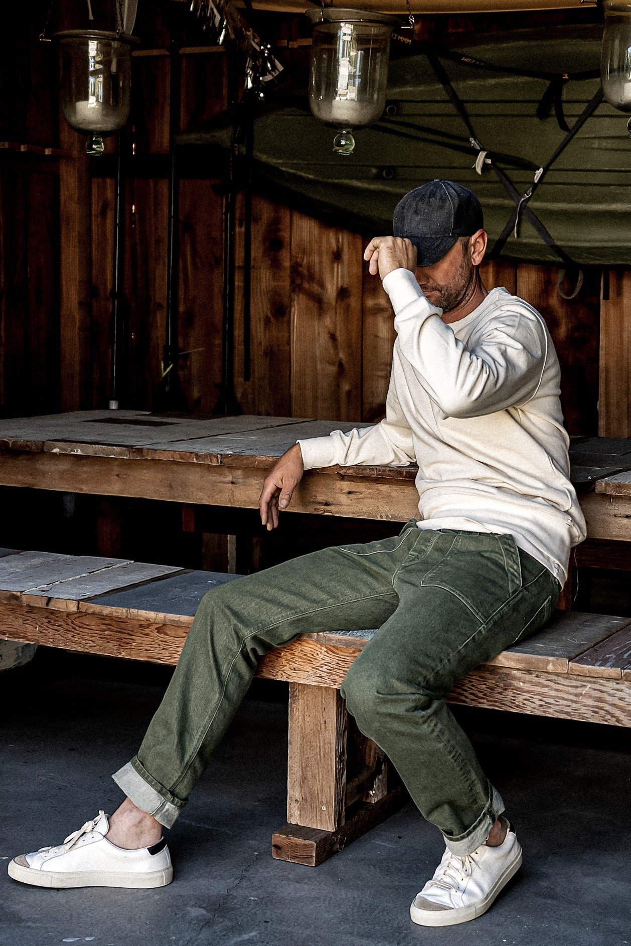 Person in olive Scout military denim pants with cuffed hems, seated on a rustic wood bench.