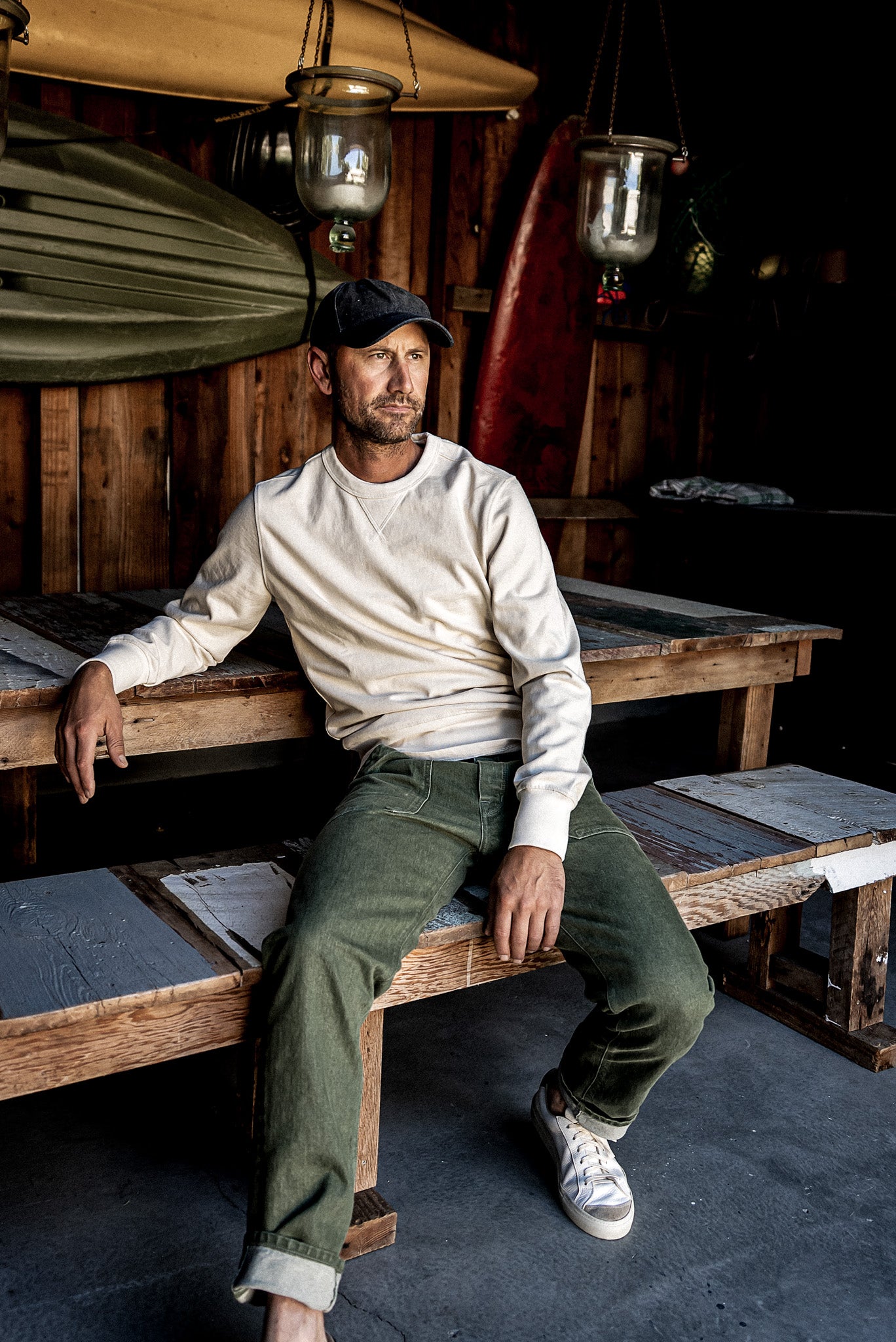 Man in olive Scout military denim jeans seated on a rustic wooden bench with cuffed hems.