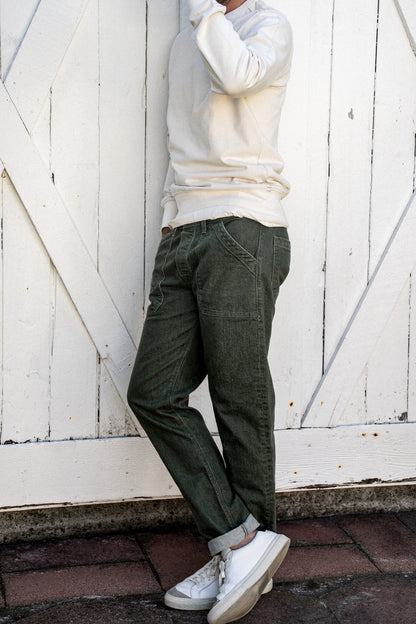 Olive Scout military denim pant with patch pockets and cuffed hem, worn against white barn doors.