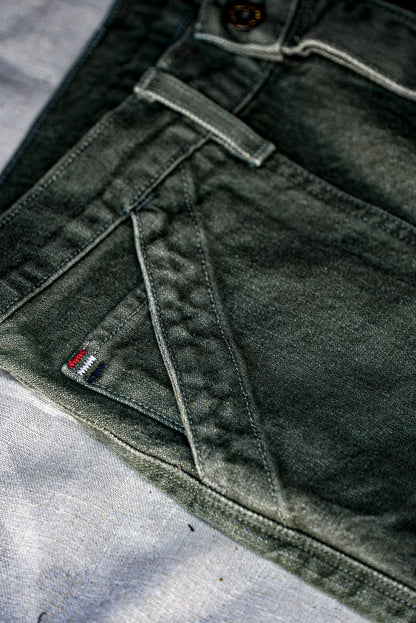 Close-up of olive broken twill denim with red, white, and blue signature bartacks and brass button.