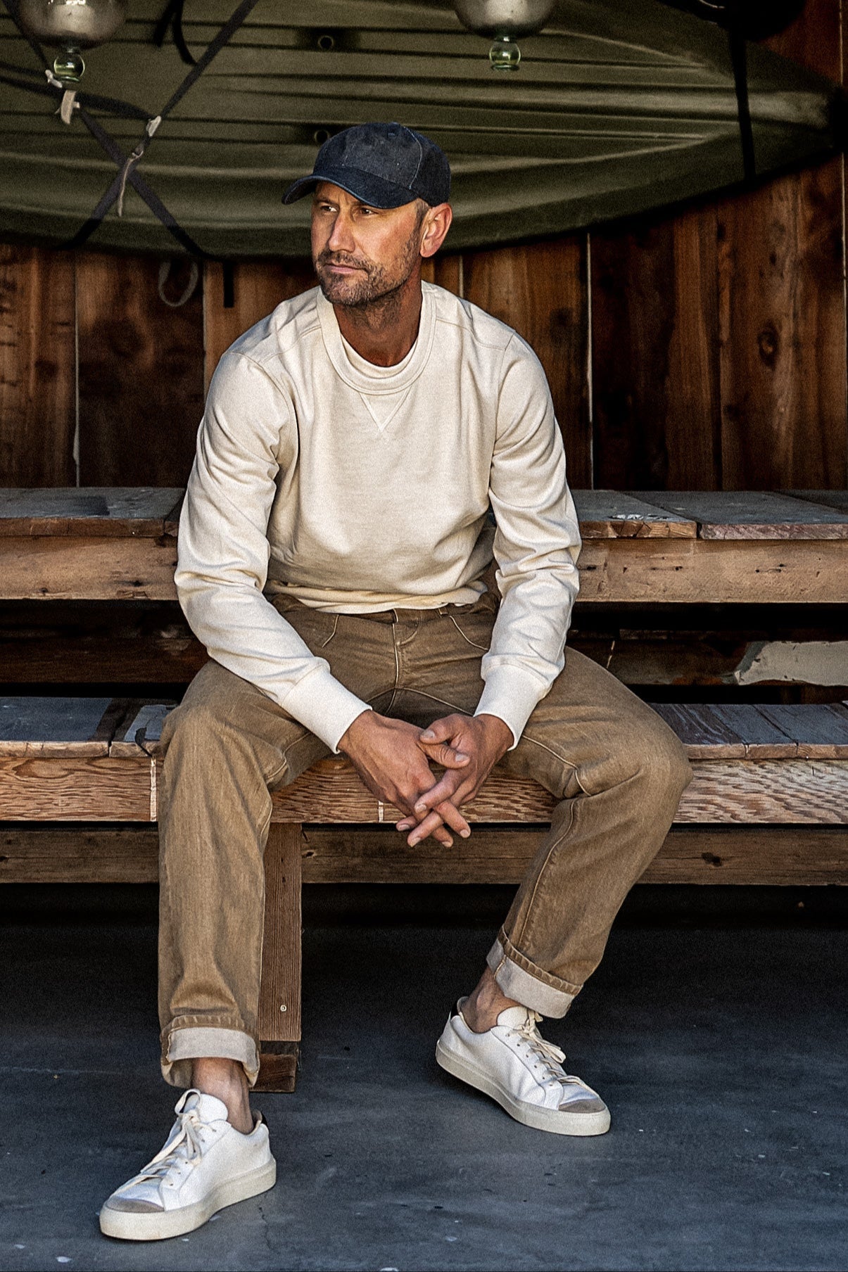 Person in wheat Scout military denim pants and cream sweatshirt, seated on wooden bench.