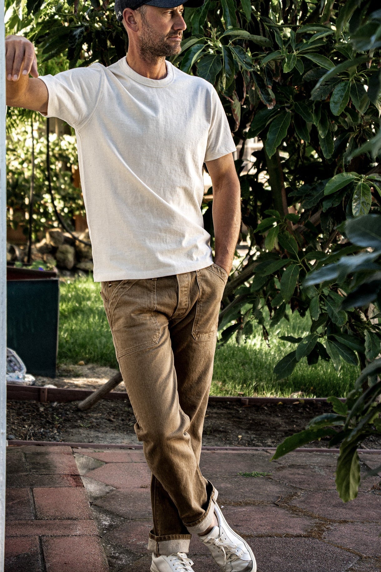 Person wearing wheat Scout military denim jeans with cuffed hems, styled with a cream tee outdoors.