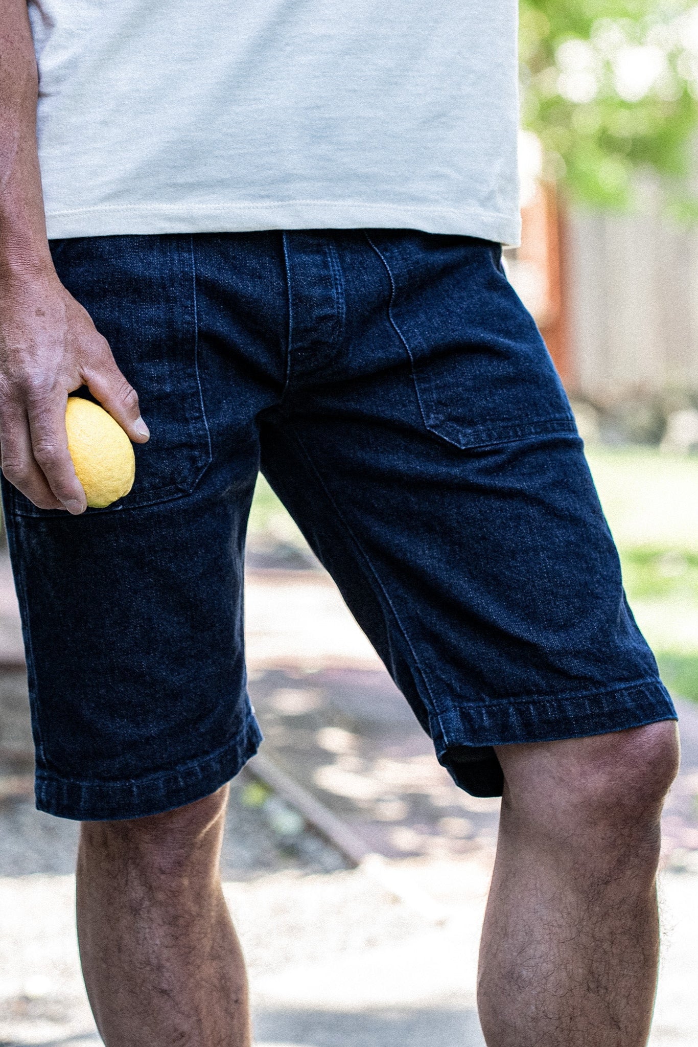Man wearing dark ocean wash denim military shorts outdoors, holding a lemon near the front pocket.
