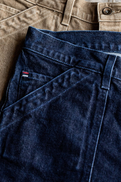 Close-up of ocean wash broken twill denim shorts folded over tan military shorts, showing waistband and stitching.
