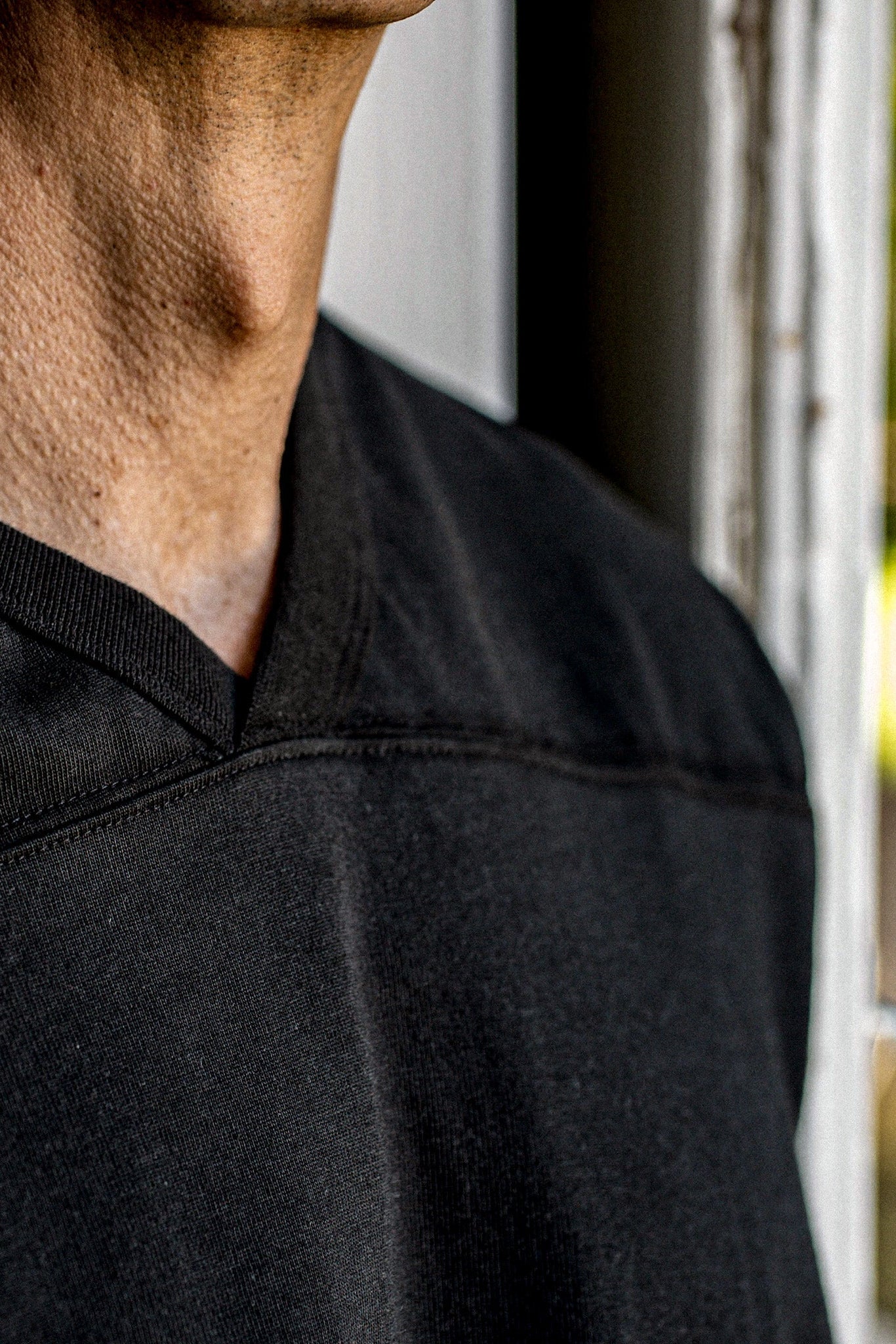 Close-up of the Stinson V-neck jersey in basalt black, showing yoke seam and neckline stitching.