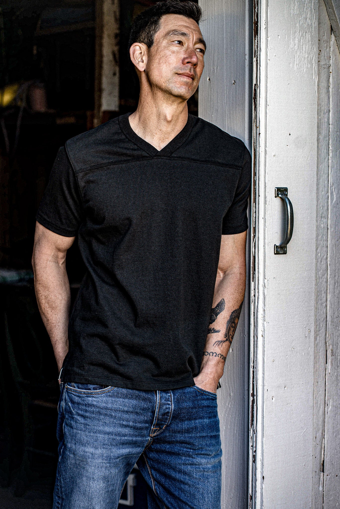 Man in Basalt Stinson V-neck cotton jersey leaning against a weathered painted door.