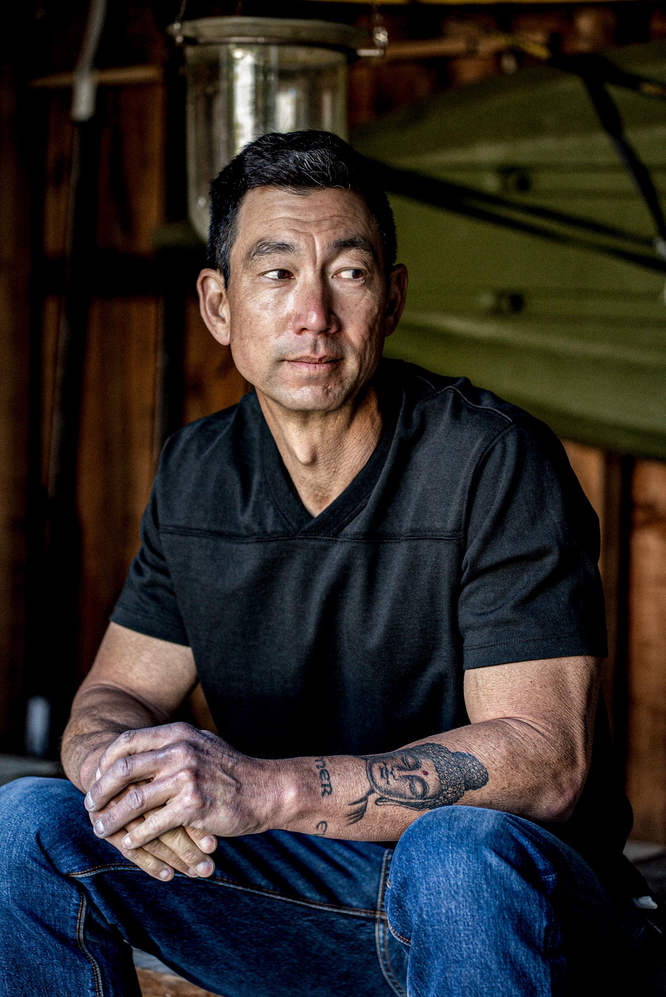 Seated man wearing a basalt 12oz cotton V-neck jersey paired with blue jeans.