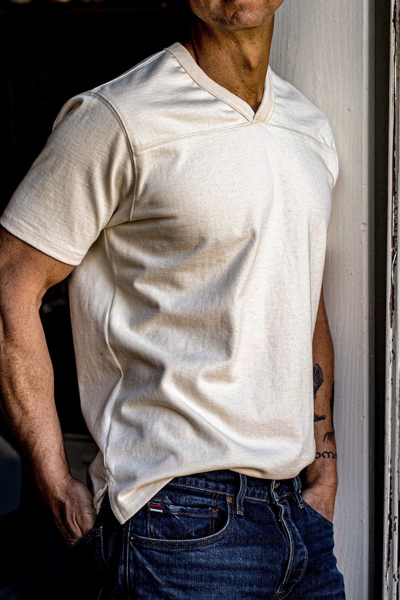 Man wearing natural cotton Stinson V-neck jersey with dark denim jeans in a doorway.
