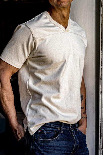 Man wearing natural cotton Stinson V-neck jersey with dark denim jeans in a doorway.