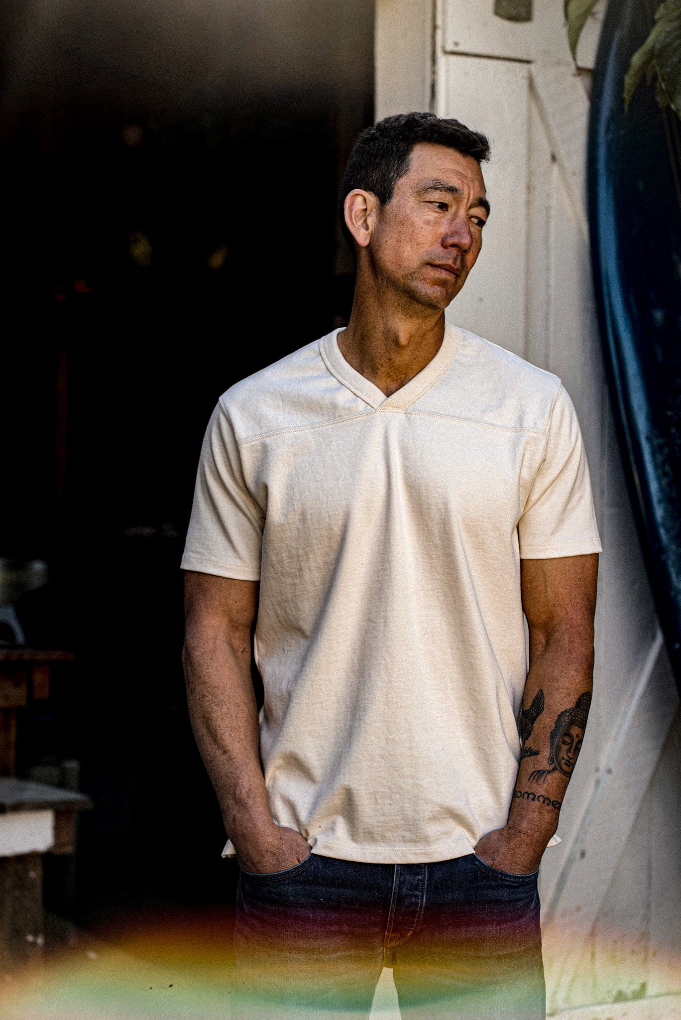 Man in natural cotton Stinson V-neck jersey tee with denim, leaning by a doorway.