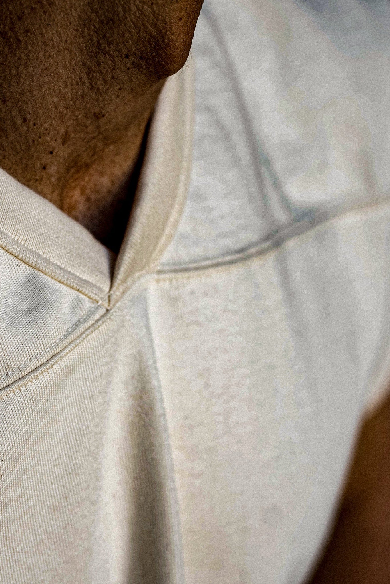Close-up of natural cotton V-neck jersey showing stitched neckline seam and yolk detail.
