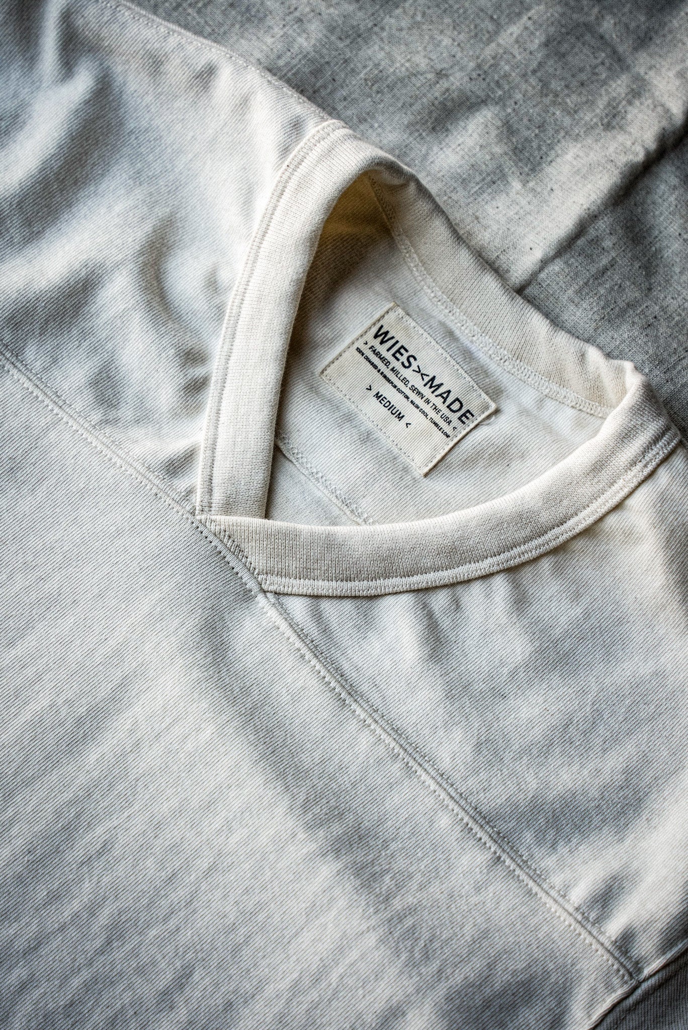 Close-up of natural cotton V-neck jersey collar with WiesMade label and yoke seam.