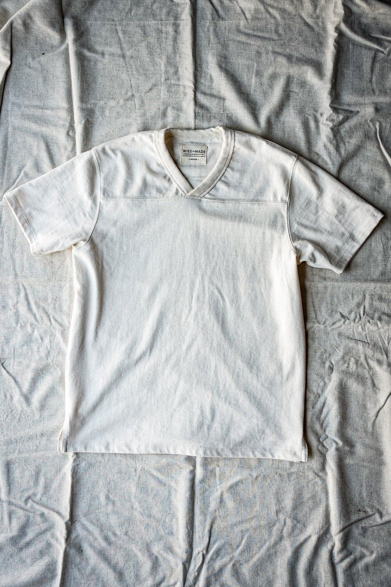 Men's natural 12oz cotton V-neck jersey tee laid flat on canvas backdrop.