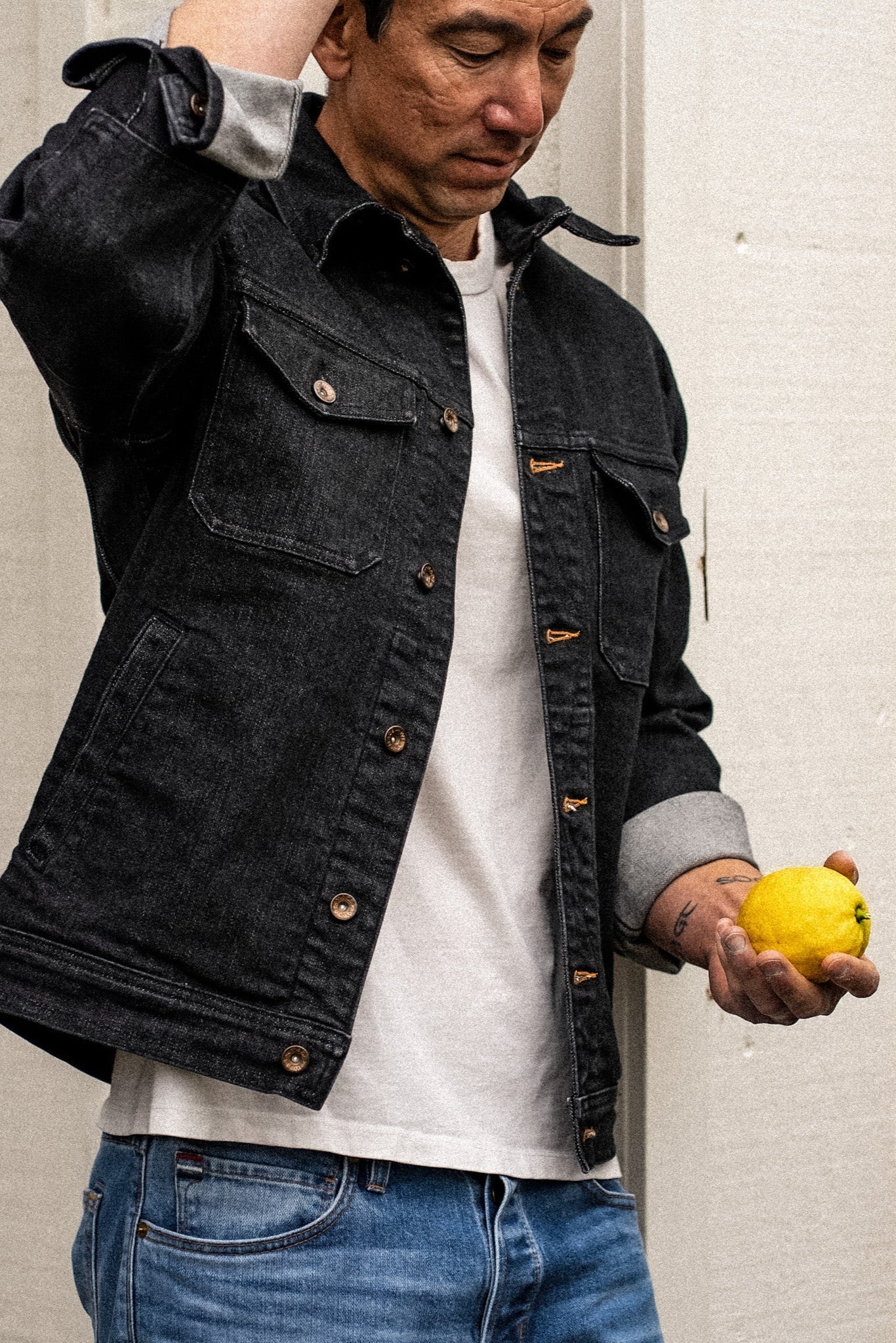 Black broken twill denim Artcher jacket worn open over a white tee, brass buttons visible.