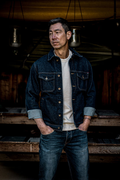 Man wearing the Artcher ocean broken twill denim jacket over a cream tee, hands in pockets.