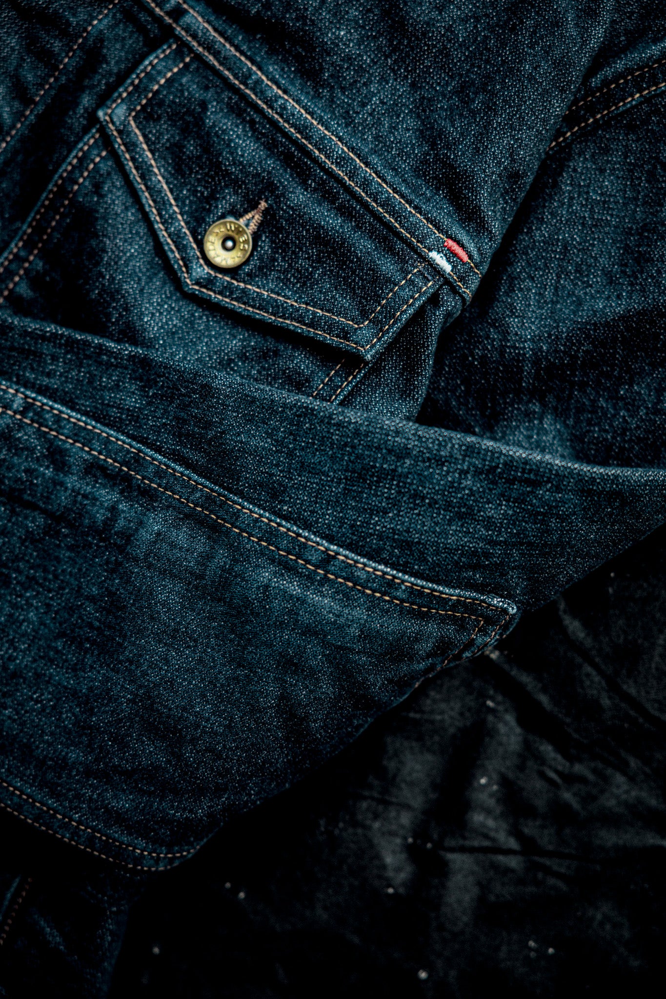 Close-up of the Artcher Jacket's 14oz broken twill denim, showing brass button pocket and contrast stitching.