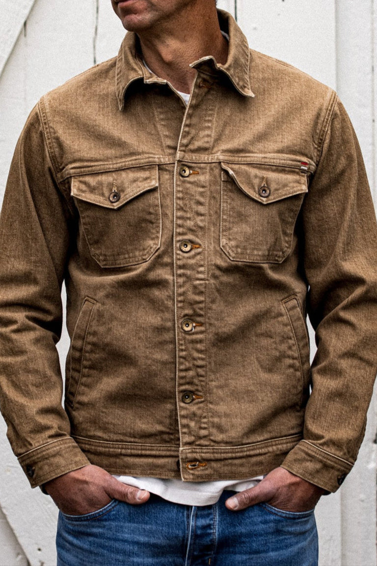 Wheat broken twill denim jacket with chest flap pockets and brass buttons, worn over a white tee.