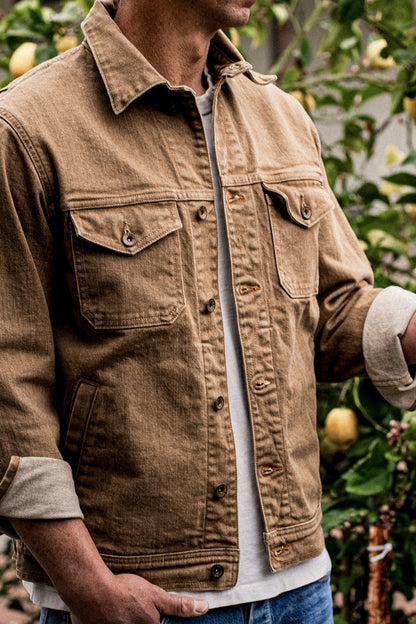 Wheat broken twill denim jacket worn open over a tee, cuffs rolled, near a lemon tree.