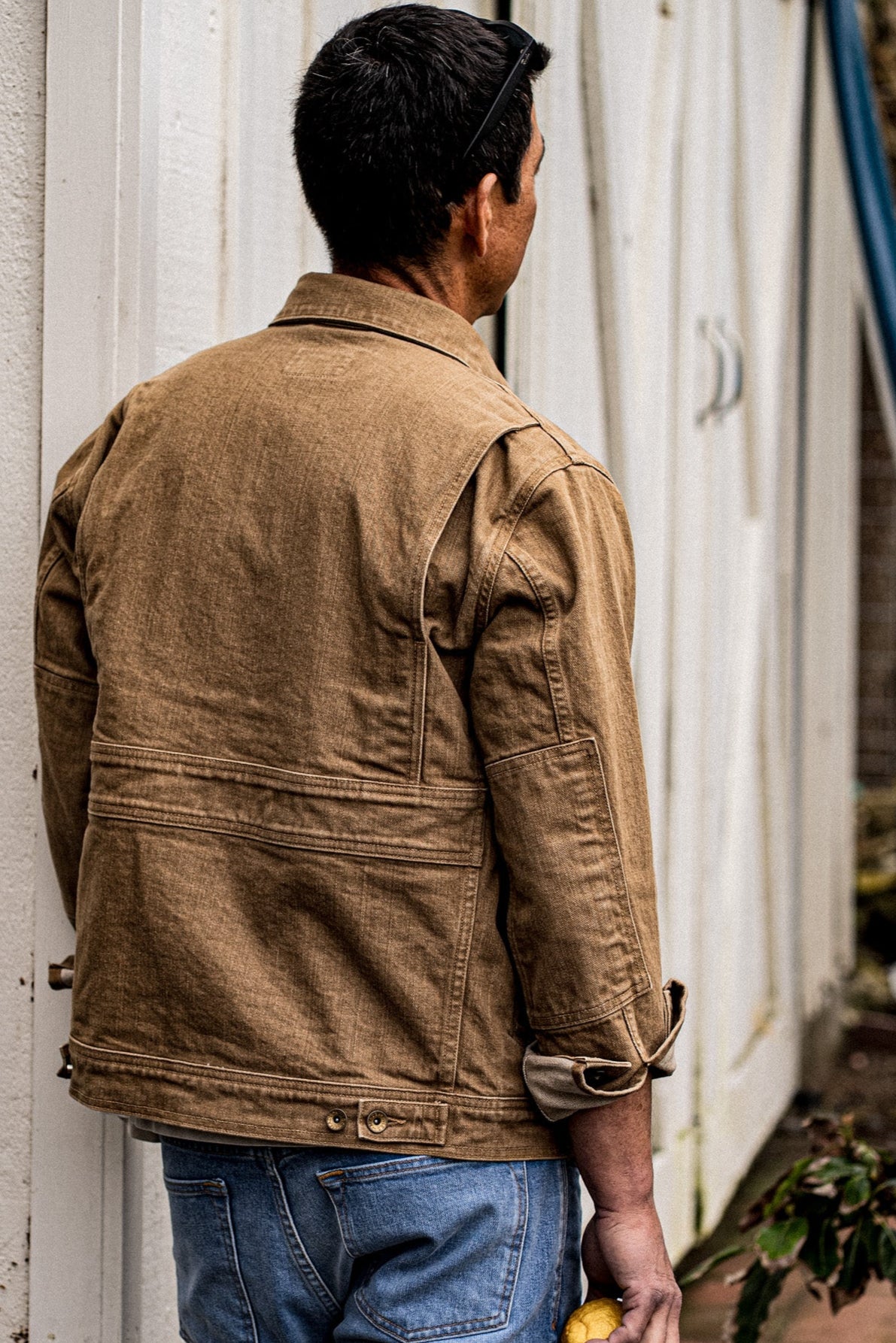 Back view of the wheat broken twill denim Artcher jacket with back gussets and cuff tabs, worn with blue jeans.