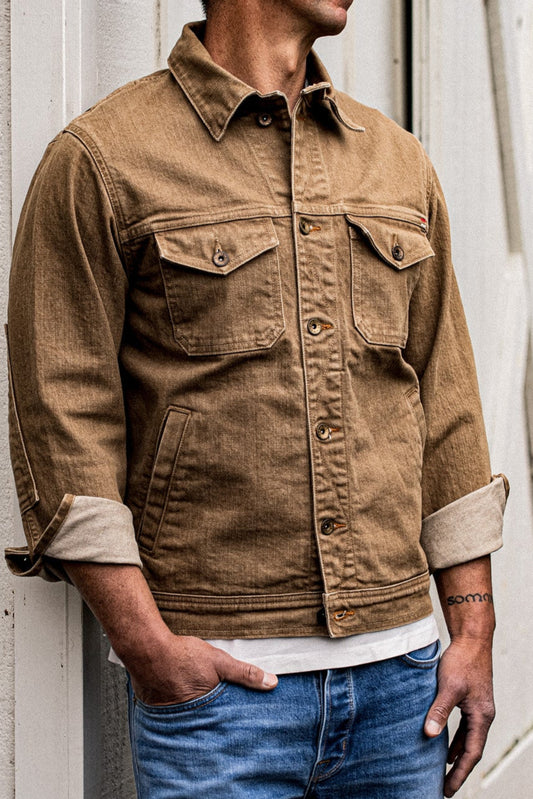 Man wearing the wheat-colored broken twill denim jacket with chest flap pockets, cuffs rolled to show contrast lining.