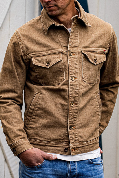 Man wearing a wheat-colored broken twill denim jacket with chest flap pockets and brass buttons.