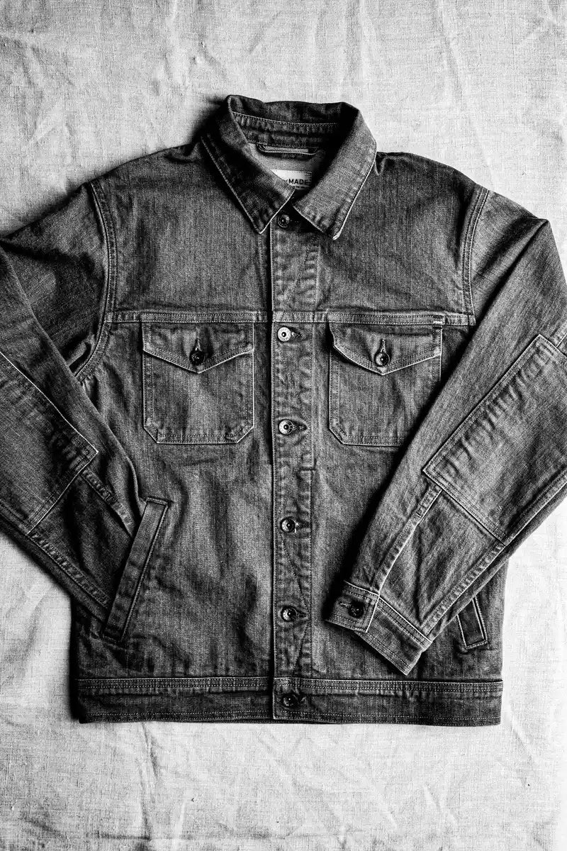 Artcher broken twill denim jacket laid flat on linen, made in USA with brass button front.