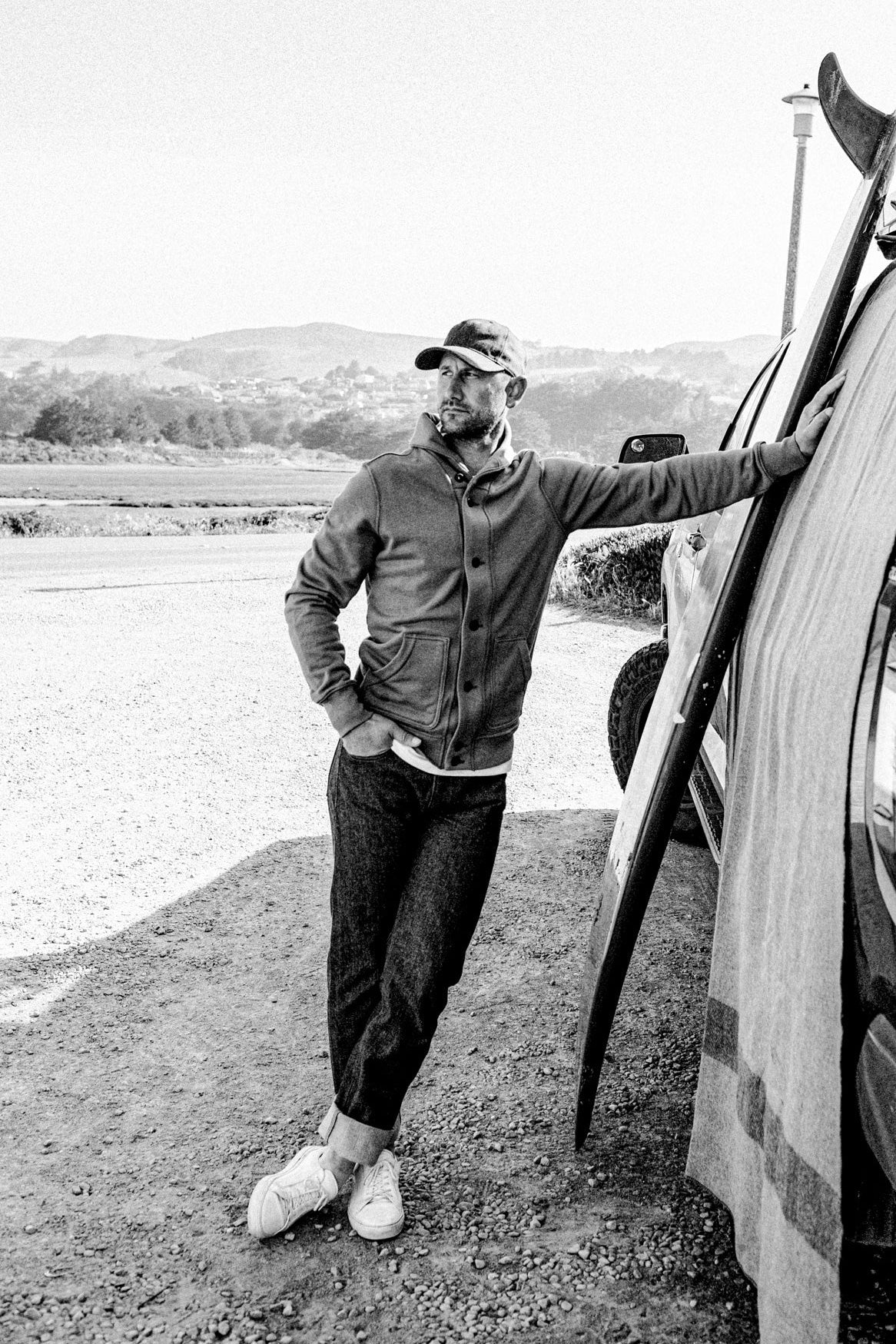 Man wearing button-up Bodega French terry cardigan and cuffed raw denim beside a truck.