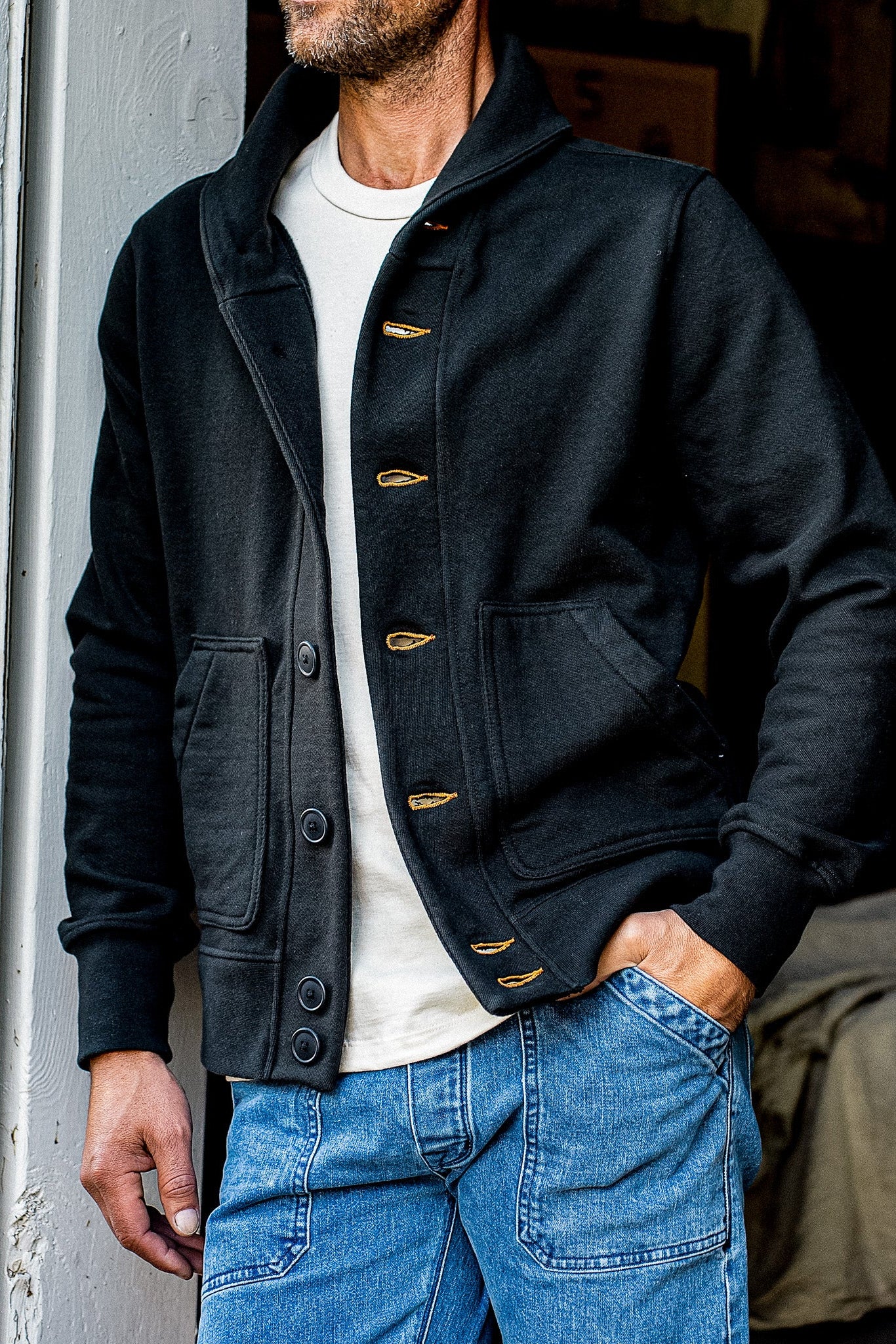 Man in a basalt French terry shawl cardigan with tobacco contrast keyholes over a cream tee.