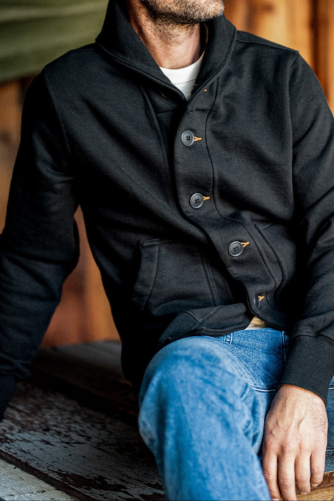 Man wearing basalt Bodega shawl cardigan with tobacco keyhole stitching and buttons over jeans.