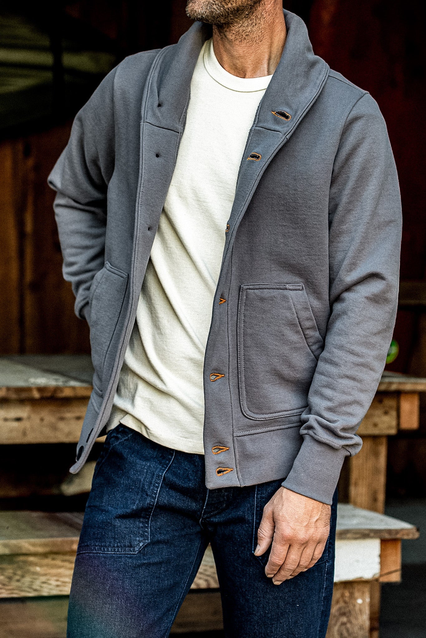 Man wearing the WiesMade Bodega grey cardigan open over a cream tee and dark jeans outdoors.