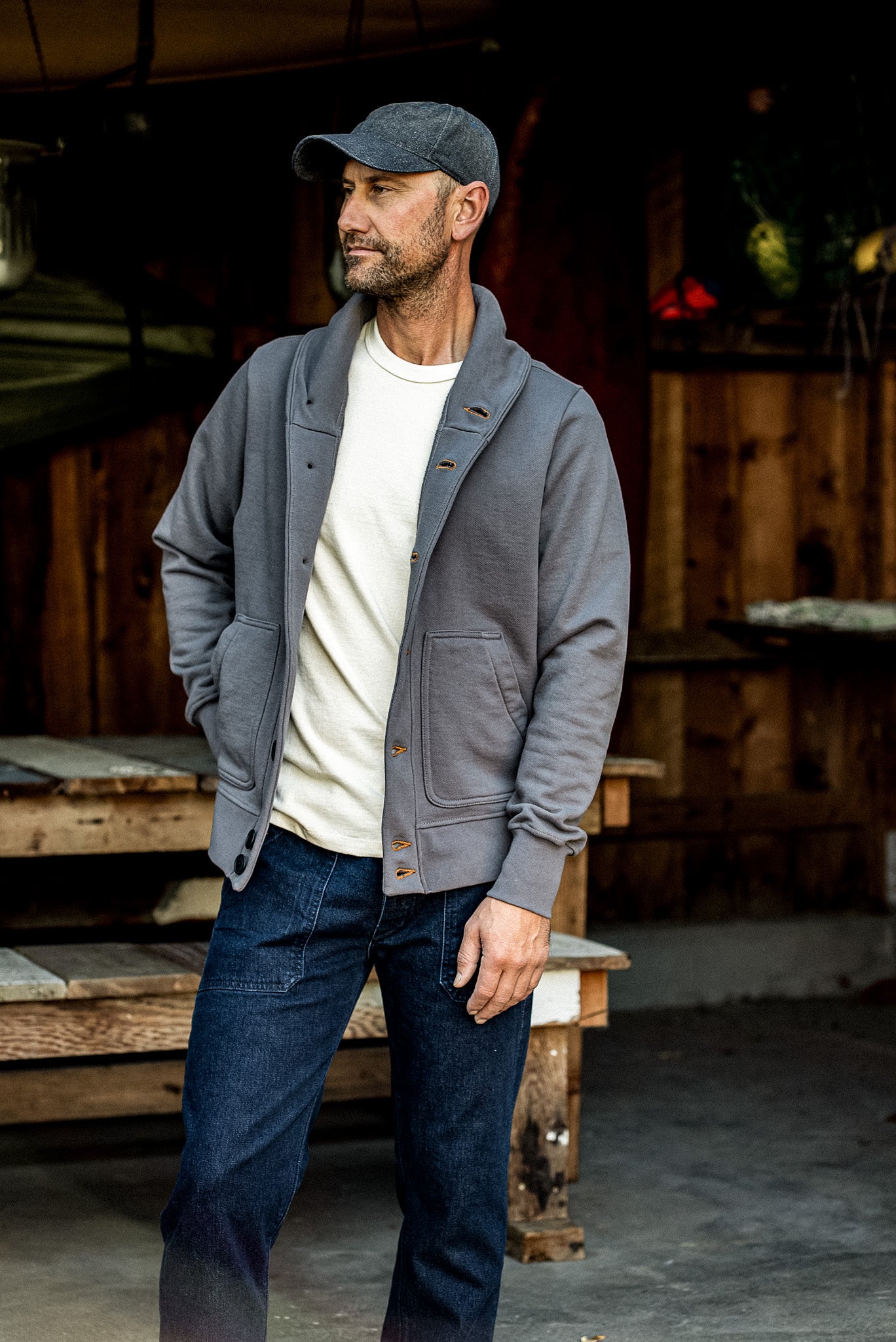 Man wearing pebble grey Bodega shawl cardigan over cream tee and dark jeans outdoors.