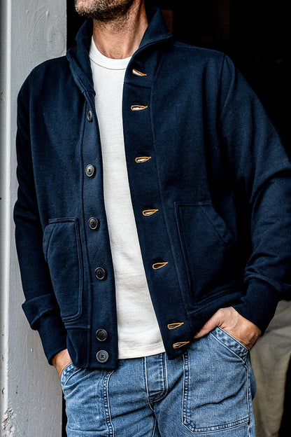 Navy French terry shawl collar cardigan with tobacco contrast keyhole stitching, worn over a cream tee with faded denim.