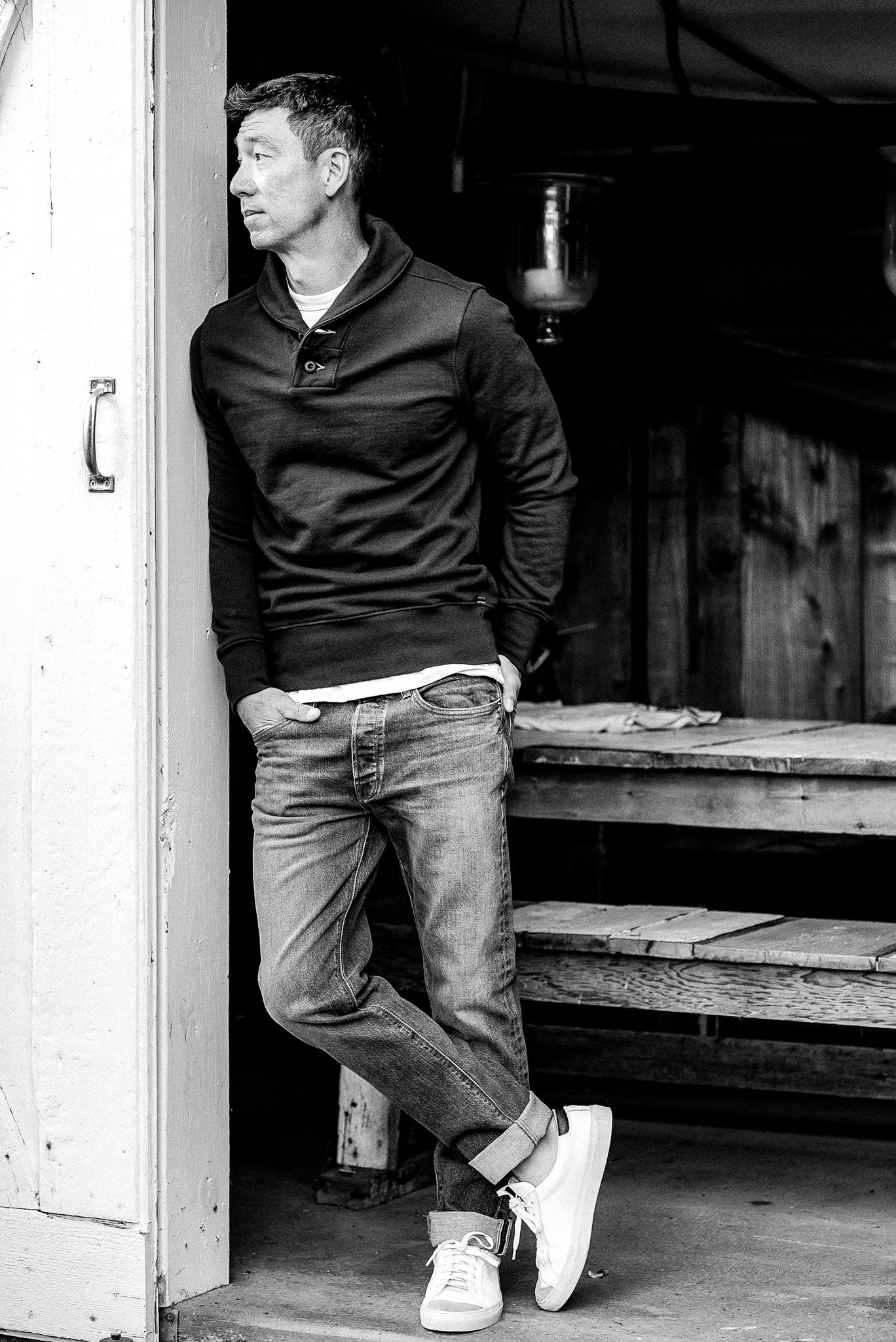 Man leaning in a doorway wearing the Bodega shawl collar French terry pullover over jeans.