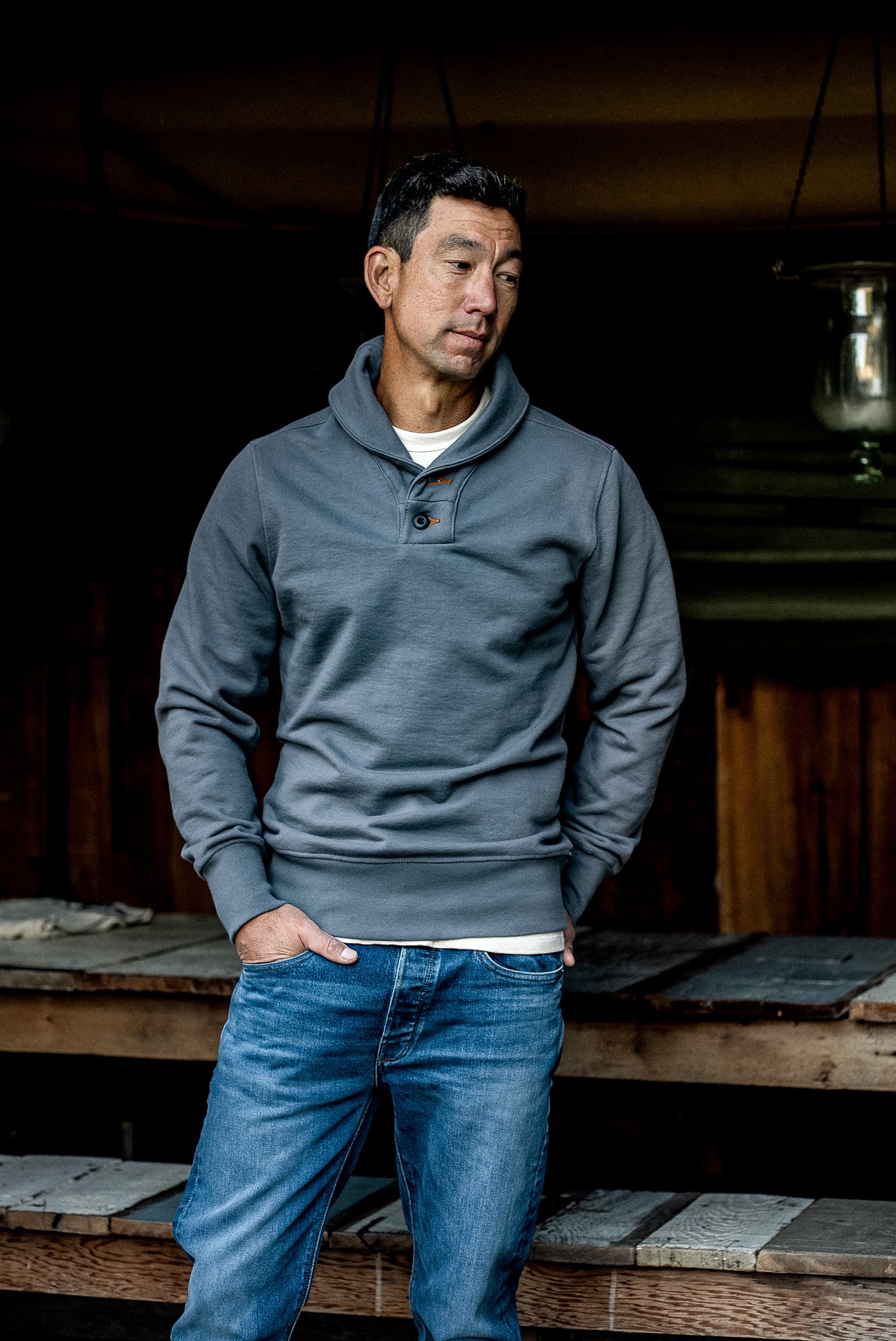 Man wearing pebble gray shawl collar pullover in heavy French terry, hands in jean pockets.