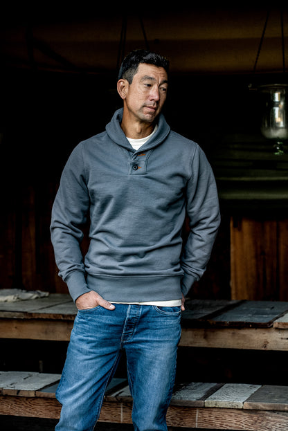 Man wearing pebble gray shawl collar pullover in heavy French terry, hands in jean pockets.
